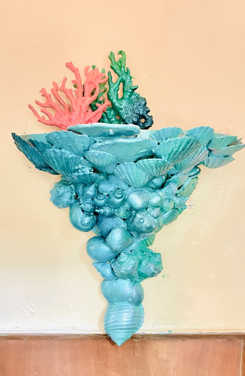 Wall bracket encrusted in teal-painted shells, topped with pink and green coral